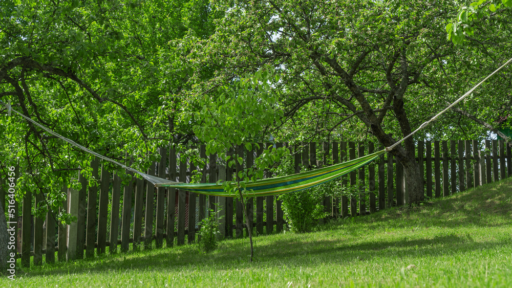 Summer garden with hanging hammock for relaxation. Hammock in backyard on the fence background. Summer garden with hanging hammock for relaxation. Hammock in backyard on the fence background.