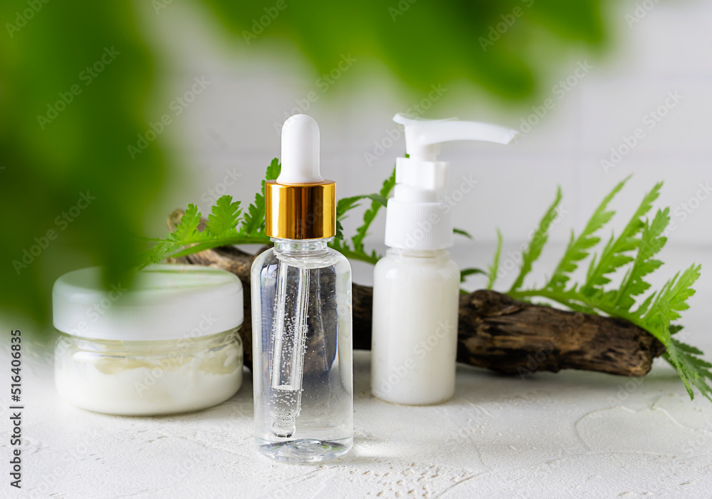 Cosmetics for face care on a bright table. Hand cream and a green twig in the background. Light background