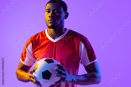 African american male soccer player with football over neon pink lighting