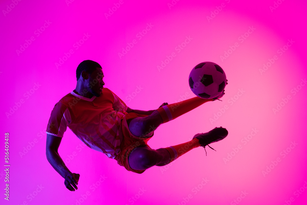 African american male soccer player kicking football over neon pink lighting African american male soccer player kicking football over neon pink lighting