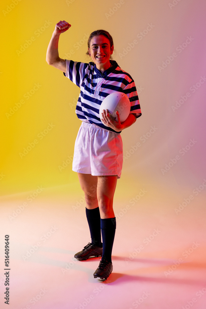 Portrait of happy caucasian female rugby player with rugby ball over neon pink lighting