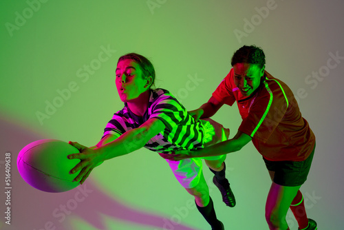 Diverse female rugby players playing rugby over neon pink lighting