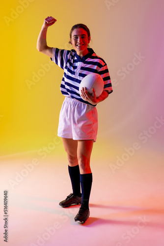 Fototapeta Naklejka Na Ścianę i Meble -  Portrait of happy caucasian female rugby player with rugby ball over neon pink lighting