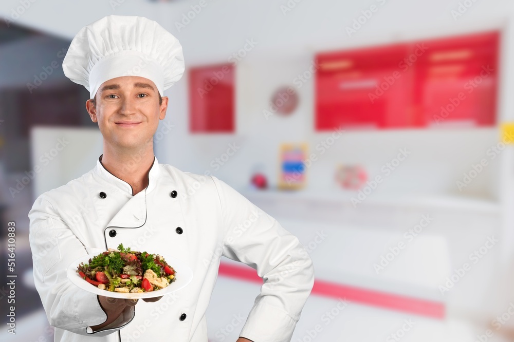 Young man standing and holding plate or dish on kitchen background Young man standing and holding plate or dish on kitchen background