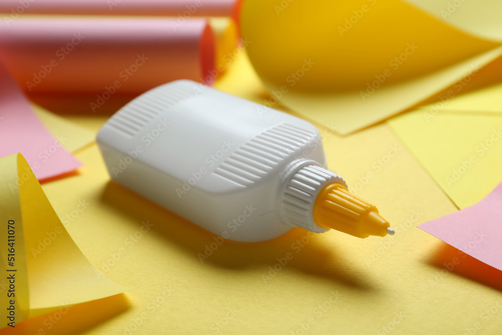 Bottle of glue and colorful paper on yellow background, closeup Bottle of glue and colorful paper on yellow background, closeup