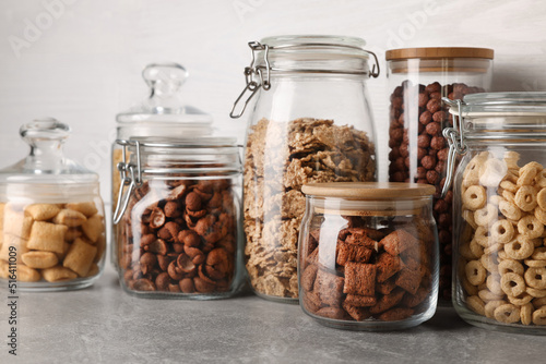 Glass containers with different breakfast cereals on grey countertop near white wooden wall
