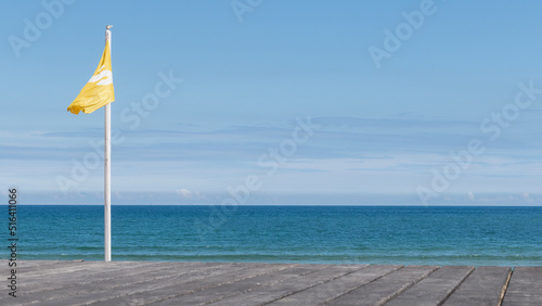 Fotografia Yellow fag on the beach. Horizon over sea. Blue sky. Danger.