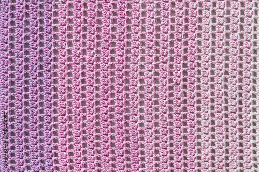 Crochet product from multicolored threads. Handmade backdrop. Flat lay. Fragment of a baktus of violet and pink tone. Striped and geometric pattern.