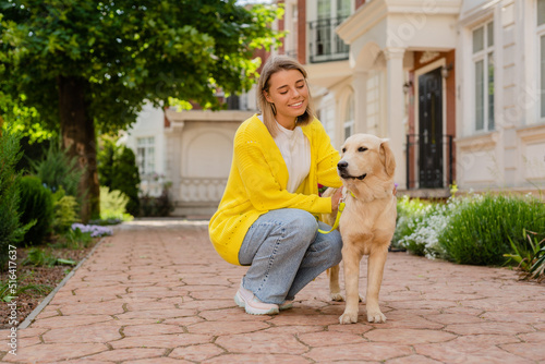 happy smiling woman in yellow sweater walking at her house with a dog golden retriever
