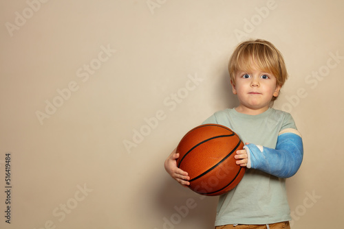 Child hold basketball ball with broken hand in plaster cast