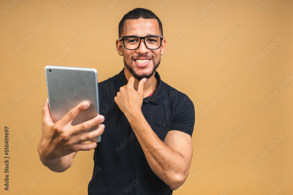 Working on digital tablet. Portrait of happy smiling young African american black man holding digital tablet while standing isolated over beige background. Working on digital tablet. Portrait of happy smiling young African american black man holding digital tablet while standing isolated over beige background.