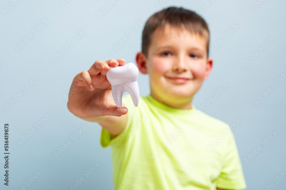 Child holds big white toy tooth on a blue background. Caring for teeth. Dentistry and healthcare concept. Healthy teeth concept Child holds big white toy tooth on a blue background. Caring for teeth. Dentistry and healthcare concept. Healthy teeth concept
