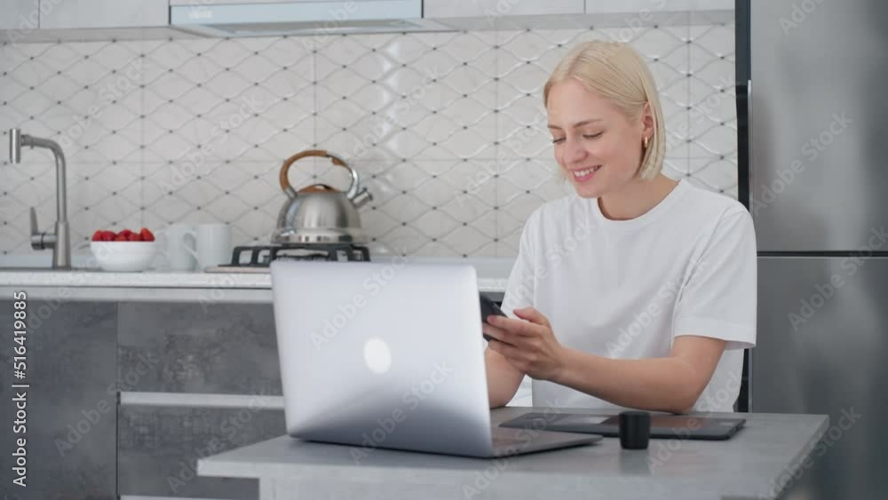 Young blonde woman looks at smartphone and smiles while working from home Young blonde woman looks at smartphone and smiles while working from home