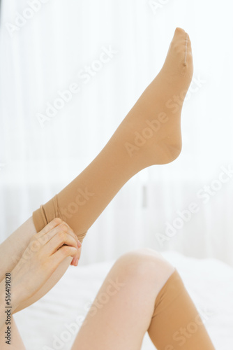 Beige compression stockings on a woman in a white room. Knee socks or socks. Girl putting on stockings at home. Beautiful female legs