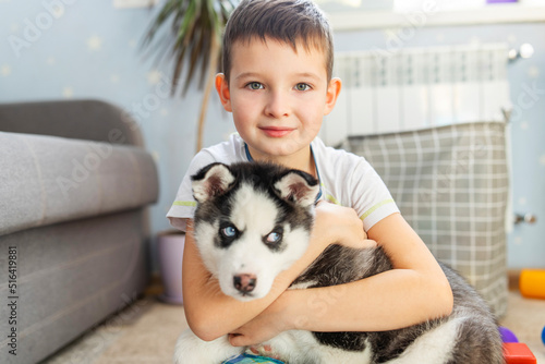 Cute child boy hugging a puppy of siberian husky dog sitting on the floor carpet at home. Love and domestic animals