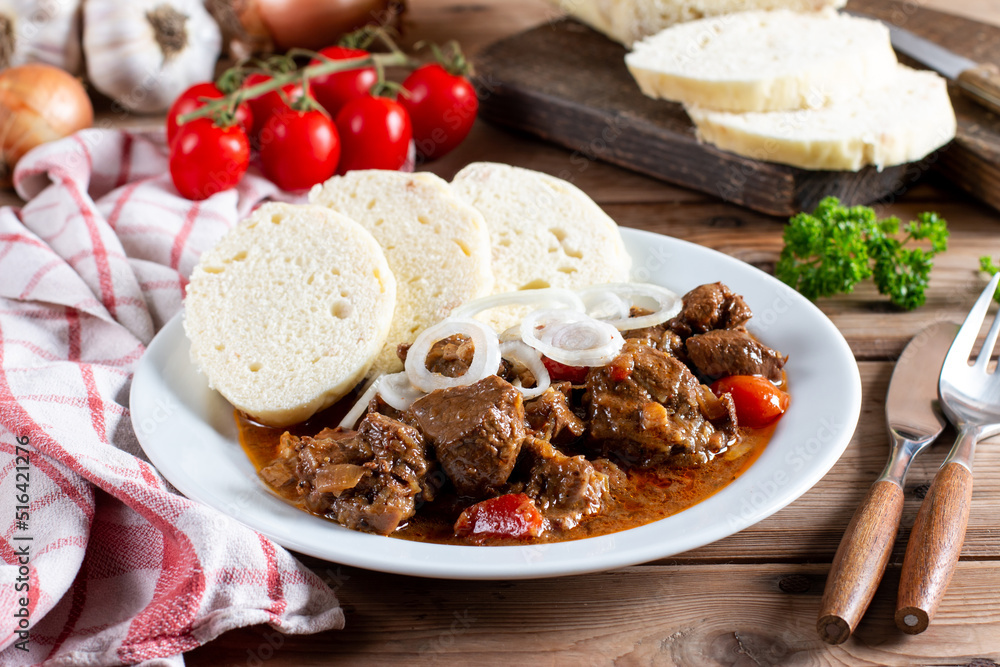 Czech traditional goulash with breaded dumpling and onion on white plate on table Czech traditional goulash with breaded dumpling and onion on white plate on table