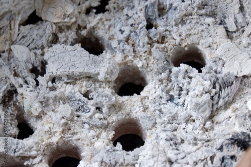 In selective focus gray ashes in a charcoal stove with many holes for background backdrop 