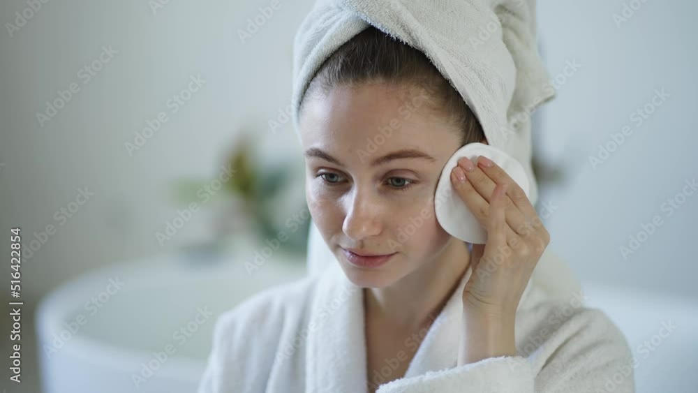 Portrait of beautiful girl in bathrobe and with towel on her head cleaning her face with sponge Portrait of beautiful girl in bathrobe and with towel on her head cleaning her face with sponge