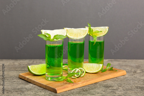 Sweet refreshing mint liqueur, with ice and mint leaves on table background, Shots with lime slice and mint flat lay photo