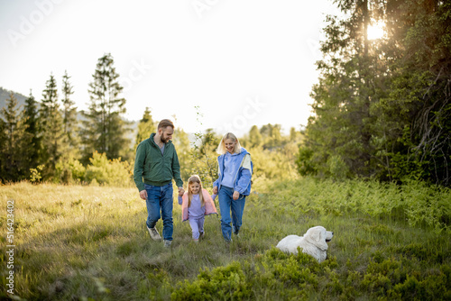 Young caucasian couple with little girl and dog walk together while traveling in the mountains. Happy family spending summer vacation on nature