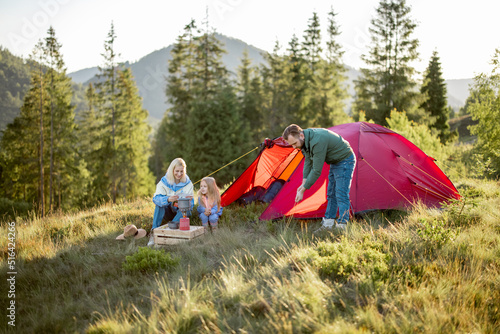 Couple with little girl have picnic at campsite while traveling with tent in the mountains. Young family happily spending vacations on nature