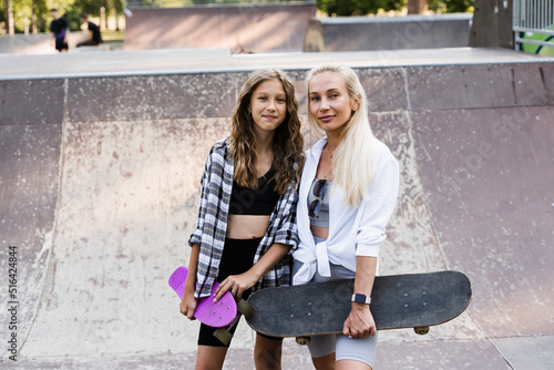 Mother and child daughter with skate and penny board training together in skate park. Extreme lifestyle. Family of mom and her kid spend time together.