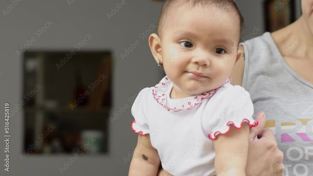 Beautiful latina baby girl with brown skin, sleepy and bored in her mother's arms. girl looking towards the street while being held by her mother. concept of motherhood. Beautiful latina baby girl with brown skin, sleepy and bored in her mother's arms. girl looking towards the street while being held by her mother. concept of motherhood.