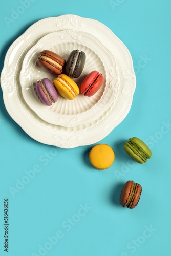 Top view of a plate of colorful macarons on a blue table and some scattered around photo