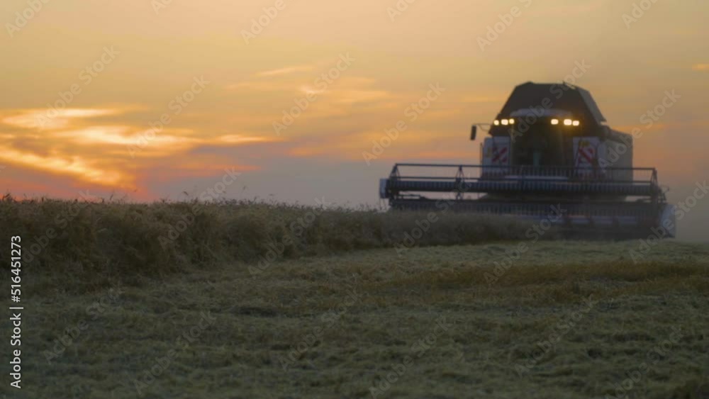 Combine Harvester Working in Field at sunset. Dusty field from the work of grain harvesting equipment. Silhouette tractor in sunlight. Seasonal Harvesting the Wheat. Agriculture. Farm. Crop. Foodstuff Combine Harvester Working in Field at sunset. Dusty field from the work of grain harvesting equipment. Silhouette tractor in sunlight. Seasonal Harvesting the Wheat. Agriculture. Farm. Crop. Foodstuff