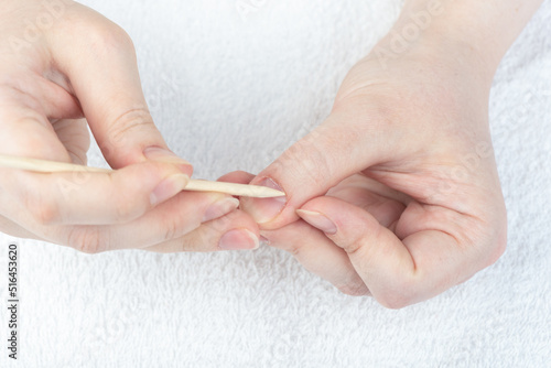 A woman corrects the cuticle on her hand with an orange stick.