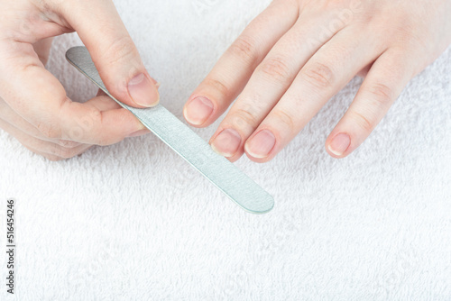 A woman corrects the shape of her nails with a nail file.
