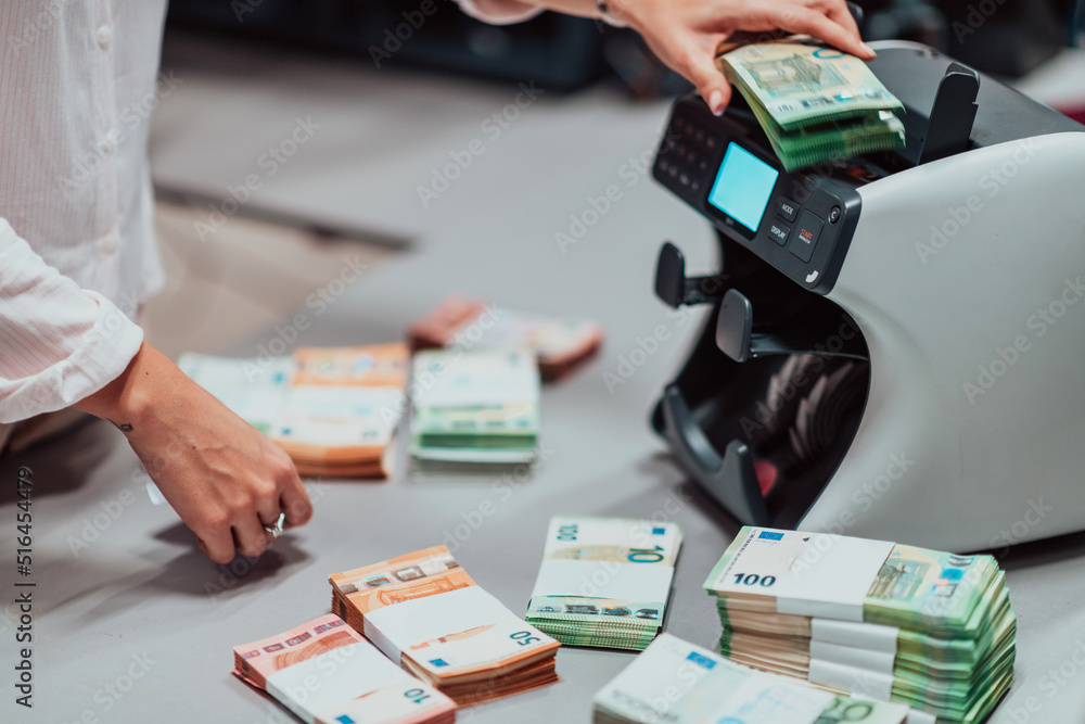 Fototapeta premium Bank employees using money counting machine while sorting and counting paper banknotes inside bank vault. Large amounts of money in the bank