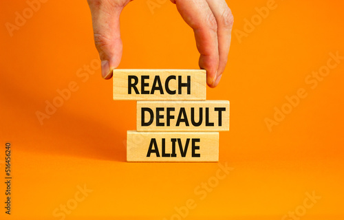 Reach default alive symbol. Concept words Reach default alive on wooden blocks on a beautiful orange table orange background. Businessman hand. Business, finacial and reach default alive concept.