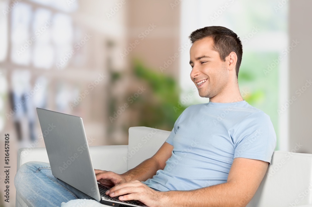 Portrait of smiling man using laptop. Adult male sitting on comfy couch in living room, watching video, taking break Portrait of smiling man using laptop. Adult male sitting on comfy couch in living room, watching video, taking break