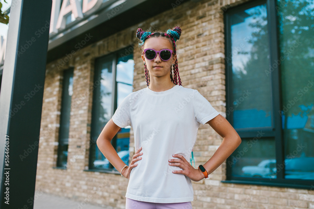 Portrait of a cute teenage girl with African braids in a white t-shirt and sunglasses stands on a city street. Mock-up for print. T-shirt template. Portrait of a cute teenage girl with African braids in a white t-shirt and sunglasses stands on a city street. Mock-up for print. T-shirt template.