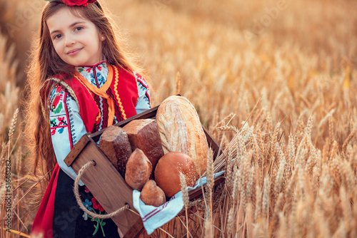 Beautiful girl woman in traditional Bulgarian folklore dress holding wicker basket with homemade breads in wheat field photo