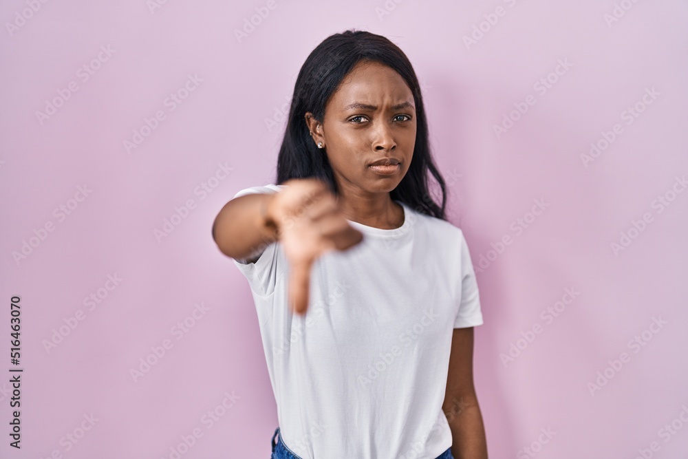 African young woman wearing casual white t shirt looking unhappy and angry showing rejection and negative with thumbs down gesture. bad expression. African young woman wearing casual white t shirt looking unhappy and angry showing rejection and negative with thumbs down gesture. bad expression.