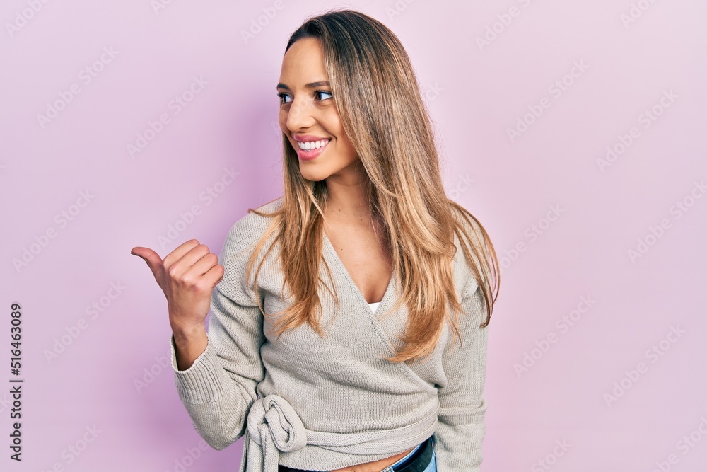 Beautiful hispanic woman wearing casual sweater pointing thumb up to the side smiling happy with open mouth Beautiful hispanic woman wearing casual sweater pointing thumb up to the side smiling happy with open mouth