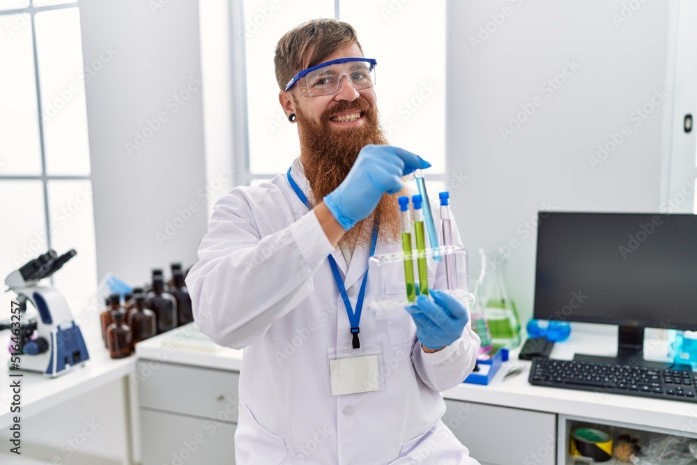 Young redhead man wearing scientist uniform holding test tubes at laboratory Young redhead man wearing scientist uniform holding test tubes at laboratory