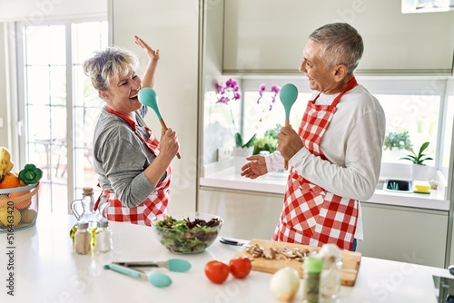 Senior caucasian couple smiling happy cooking at the kitchen.