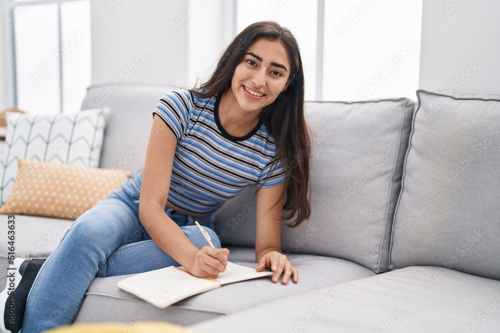 Young hispanic girl writing on notebook sitting on sofa at home Young hispanic girl writing on notebook sitting on sofa at home