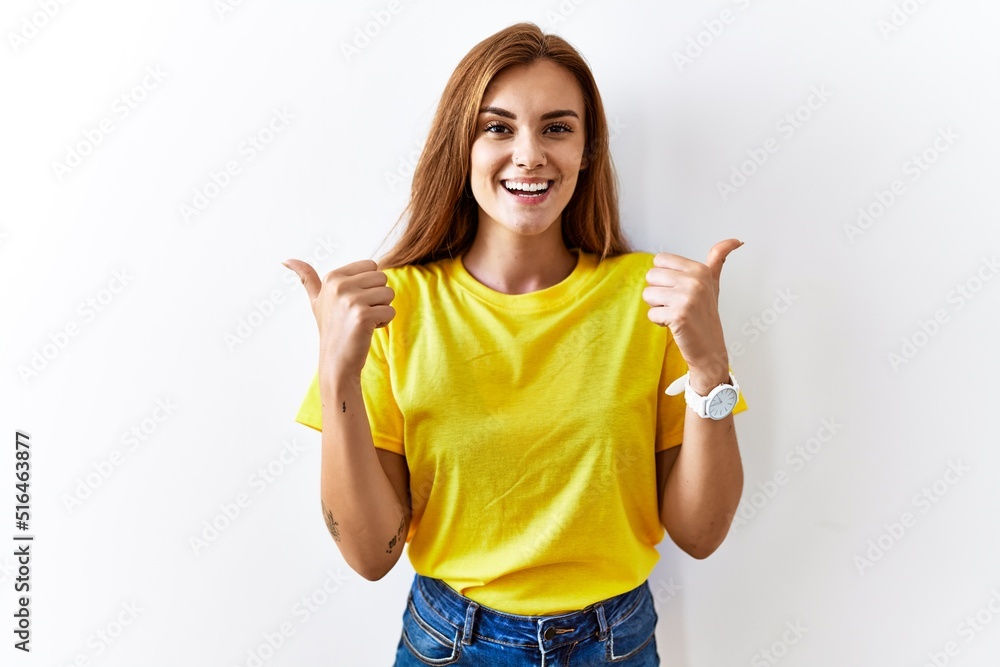 Young brunette woman standing over isolated background success sign doing positive gesture with hand, thumbs up smiling and happy. cheerful expression and winner gesture. Young brunette woman standing over isolated background success sign doing positive gesture with hand, thumbs up smiling and happy. cheerful expression and winner gesture.