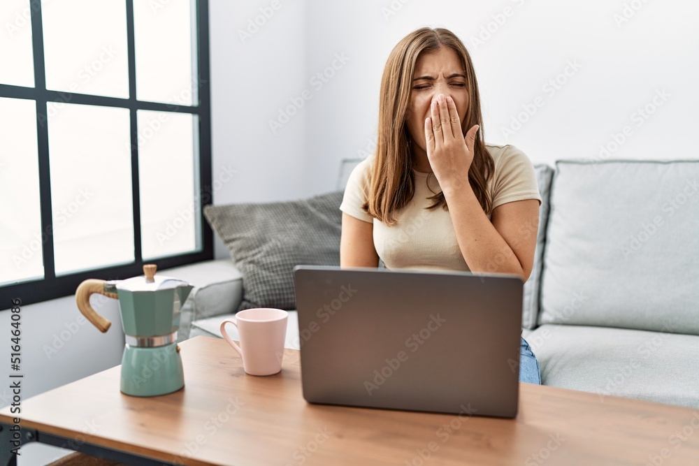 Young brunette woman using laptop at home drinking a cup of coffee bored yawning tired covering mouth with hand. restless and sleepiness. Young brunette woman using laptop at home drinking a cup of coffee bored yawning tired covering mouth with hand. restless and sleepiness.