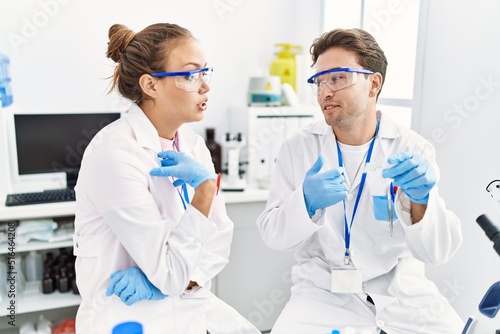Man and woman wearing scientist uniform holding sample talking at laboratory