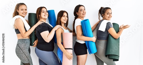 Group of women holding yoga mat standing over isolated background pointing aside with hands open palms showing copy space, presenting advertisement smiling excited happy © Krakenimages.com