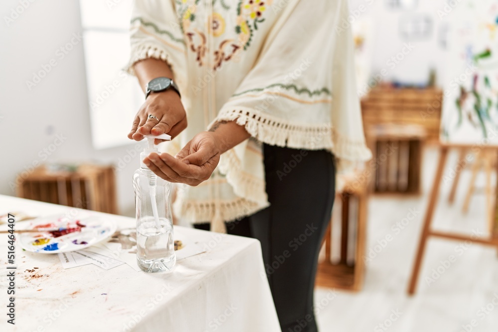 Fototapeta premium Young hispanic woman using sanitizer gel hands at art studio