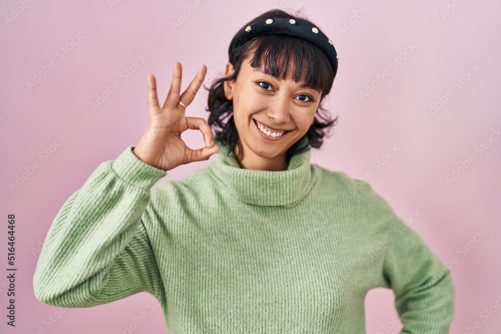 Young beautiful woman standing over pink background smiling positive doing ok sign with hand and fingers. successful expression. Young beautiful woman standing over pink background smiling positive doing ok sign with hand and fingers. successful expression.