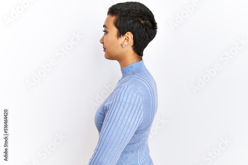 Young hispanic woman with short hair standing over isolated background looking to side, relax profile pose with natural face with confident smile.