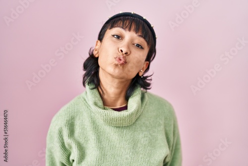 Young beautiful woman standing over pink background looking at the camera blowing a kiss on air being lovely and sexy. love expression.