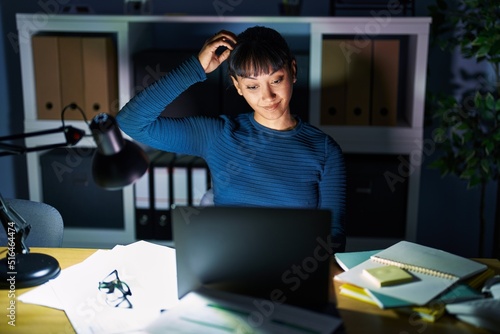 Young beautiful woman working at the office at night confuse and wonder about question. uncertain with doubt, thinking with hand on head. pensive concept.